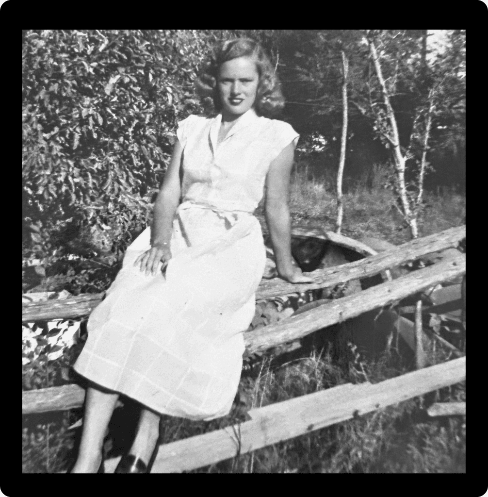 Black and white photo of a young woman named Annette, Linda's mother-in-law, sitting casually on a rustic wooden fence outdoors.