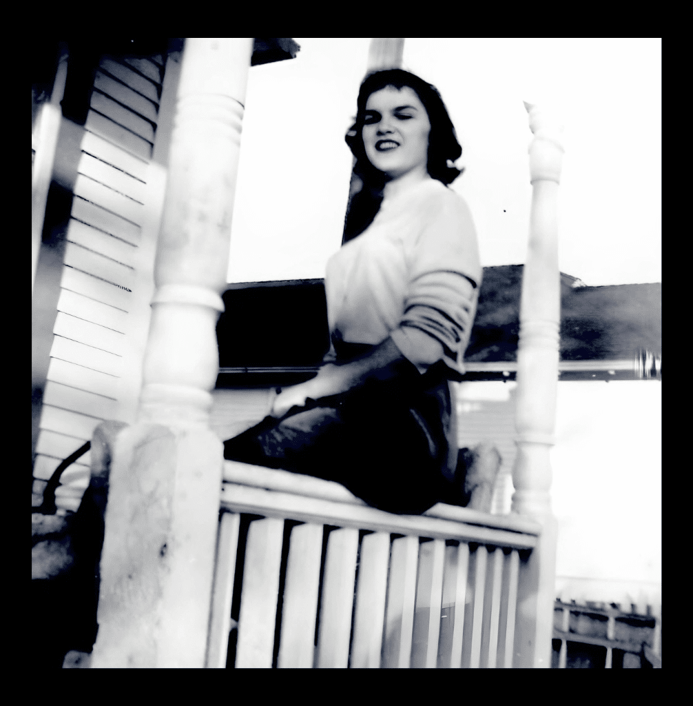Ruthie, a young brunette woman, sitting casually on a front porch railing in a 1950s black and white photo.